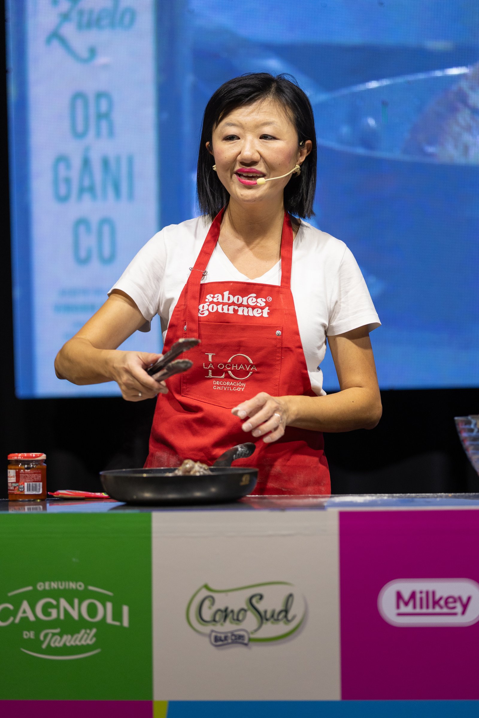 Karina Gao sonriendo mientras cocina con una sartén en el escenario