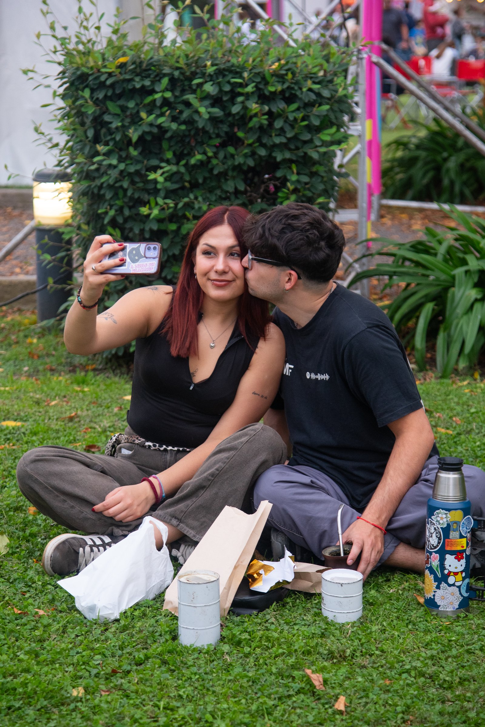 Pareja sacándose una selfie sentada en el pasto mientras toman mate
