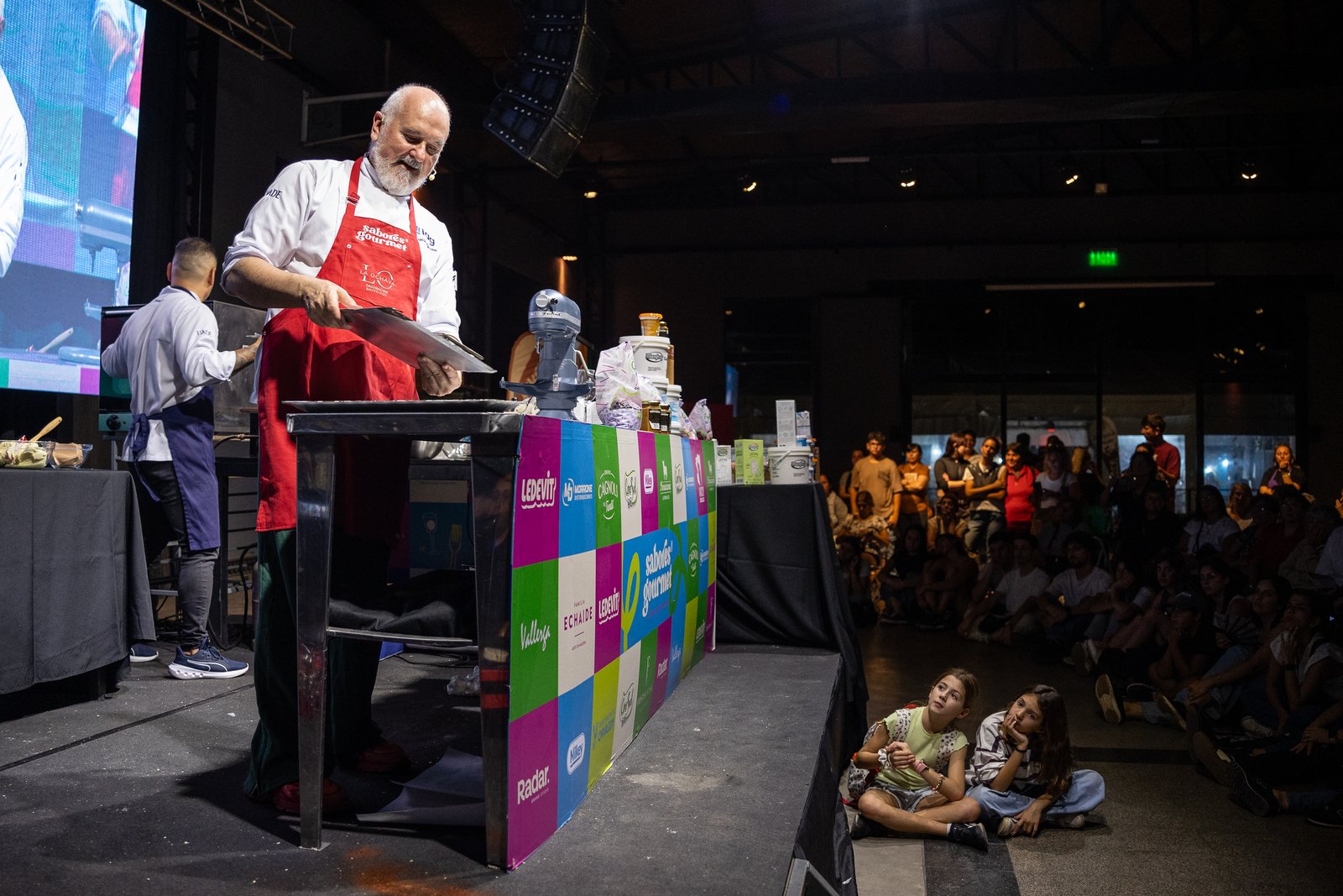 Chef con barba blanca sacándose una selfie sobre el escenario junto a otros cocineros